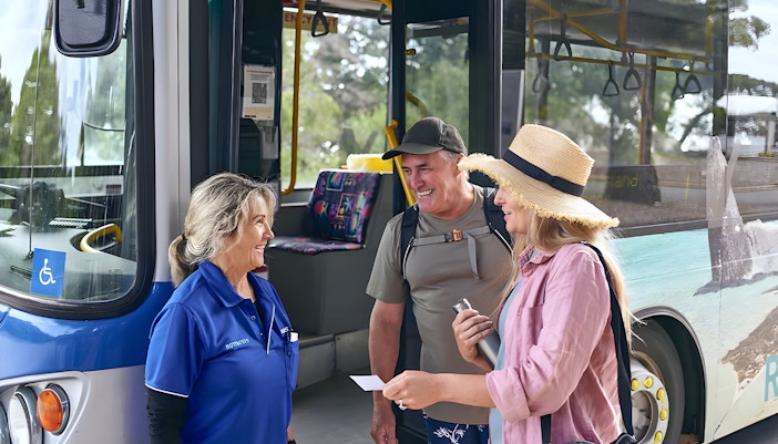 Group of tourists enjoying a sunny day on the Rottnest Island Guided Bus Tour, with a return ferry visible in the background, departing from Perth or Fremantle