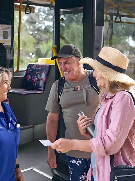 Tourists boarding a bus, assisted by a staff member, with luggage in the background.
