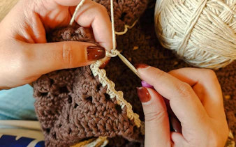 Crocheting with brown and beige yarn at a workshop in Safi, Essaouira.
