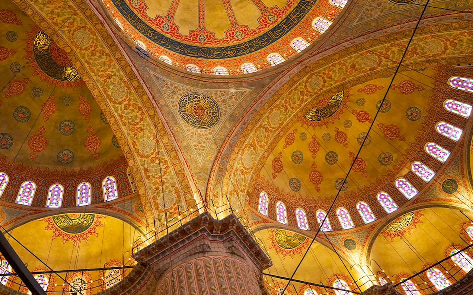 Interior view of the Blue Mosque's ornate ceiling with intricate patterns and stained glass windows.