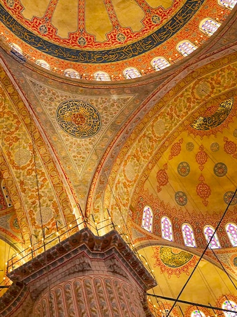 Interior view of the Blue Mosque's ornate ceiling with intricate patterns and stained glass windows.