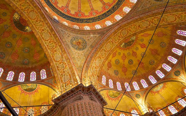 Interior view of the Blue Mosque's ornate ceiling with intricate patterns and stained glass windows.