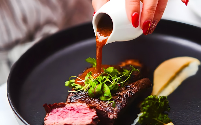 Steak with sauce being poured, garnished with greens, on the Gold Penfolds Dinner Cruise, Sydney Harbour.