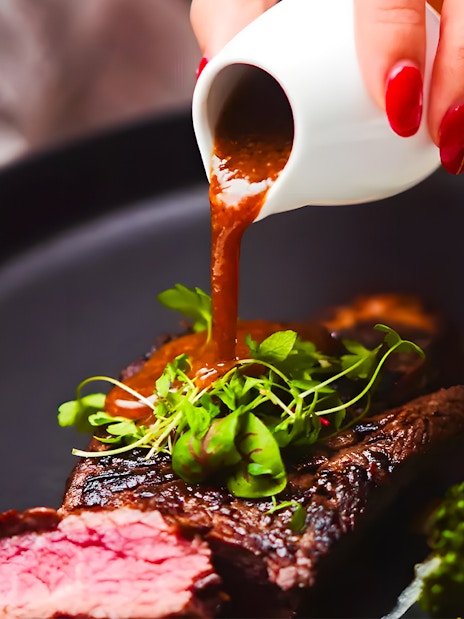 Steak with sauce being poured, garnished with greens, on the Gold Penfolds Dinner Cruise, Sydney Harbour.
