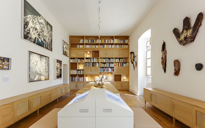 Interior of Beaulieu-en-Rouergue Abbey library with art displays and wooden bookshelves.