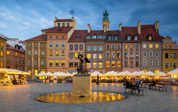 Warsaw Old Town square with mermaid statue and colorful buildings at dusk.
