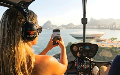 Tourist capturing view of Rio de Janeiro from helicopter, featuring Sugarloaf Mountain.