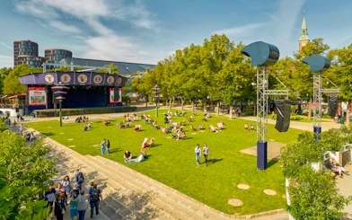 Visitors relaxing on the lawn at Tivoli Gardens, Copenhagen, with nearby attractions and rides.