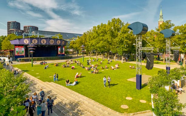 Visitors relaxing on the lawn at Tivoli Gardens, Copenhagen, with nearby attractions and rides.