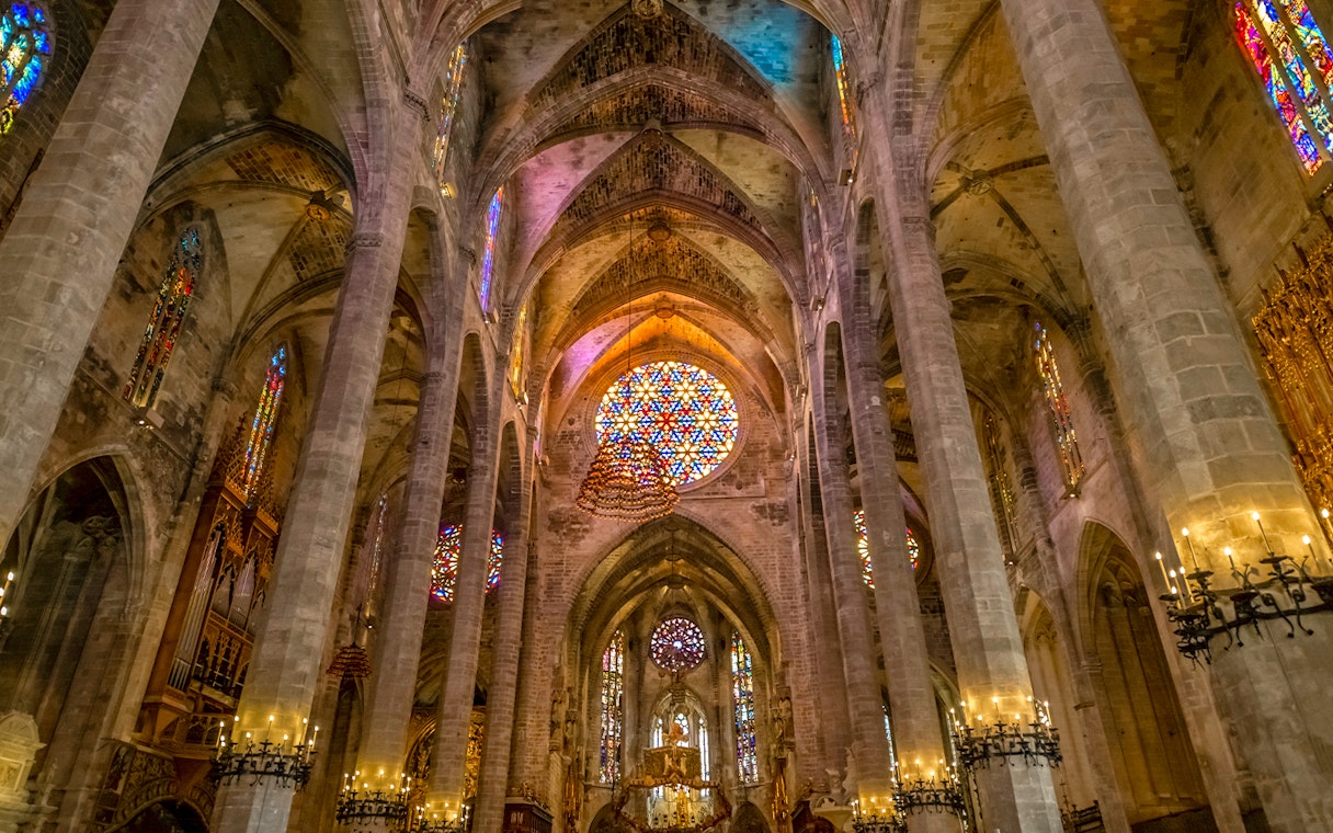 Gothic interior with stained glass windows and columns in Palma Cathedral.