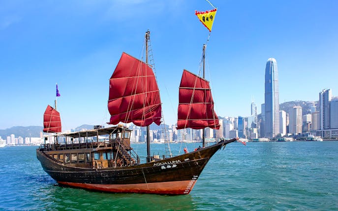 AquaLuna junk boat sailing in Hong Kong Harbor with city skyline in the background.