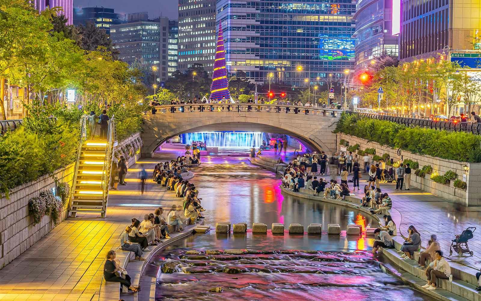 Cheonggyecheon Stream in Seoul at night with people walking and sitting along the illuminated waterway.