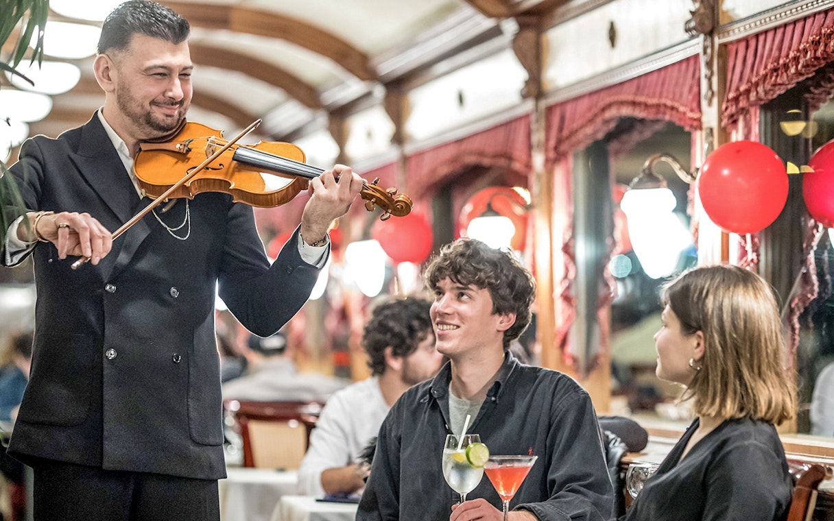 Guests enjoying live violin music and drinks on Danube sightseeing cruise.