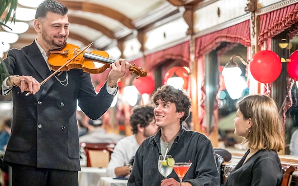Guests enjoying live violin music and drinks on Danube sightseeing cruise.
