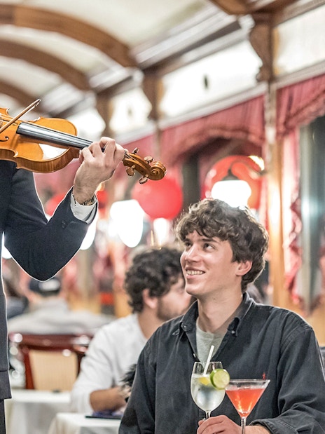 Guests enjoying live violin music and drinks on Danube sightseeing cruise.