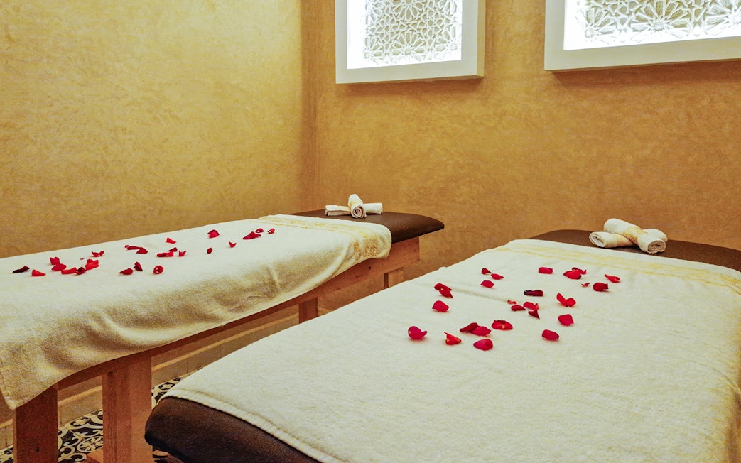 Spa treatment room with two massage tables, rose petals, and rolled towels.