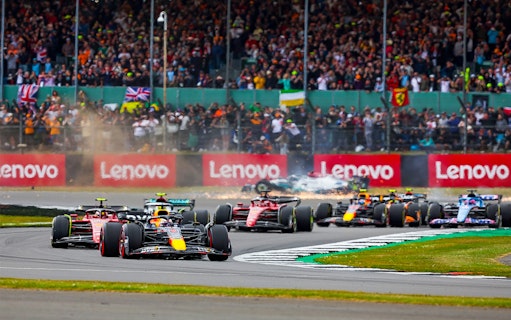 Formula 1 cars racing at the British Grand Prix with a cheering crowd in the background.