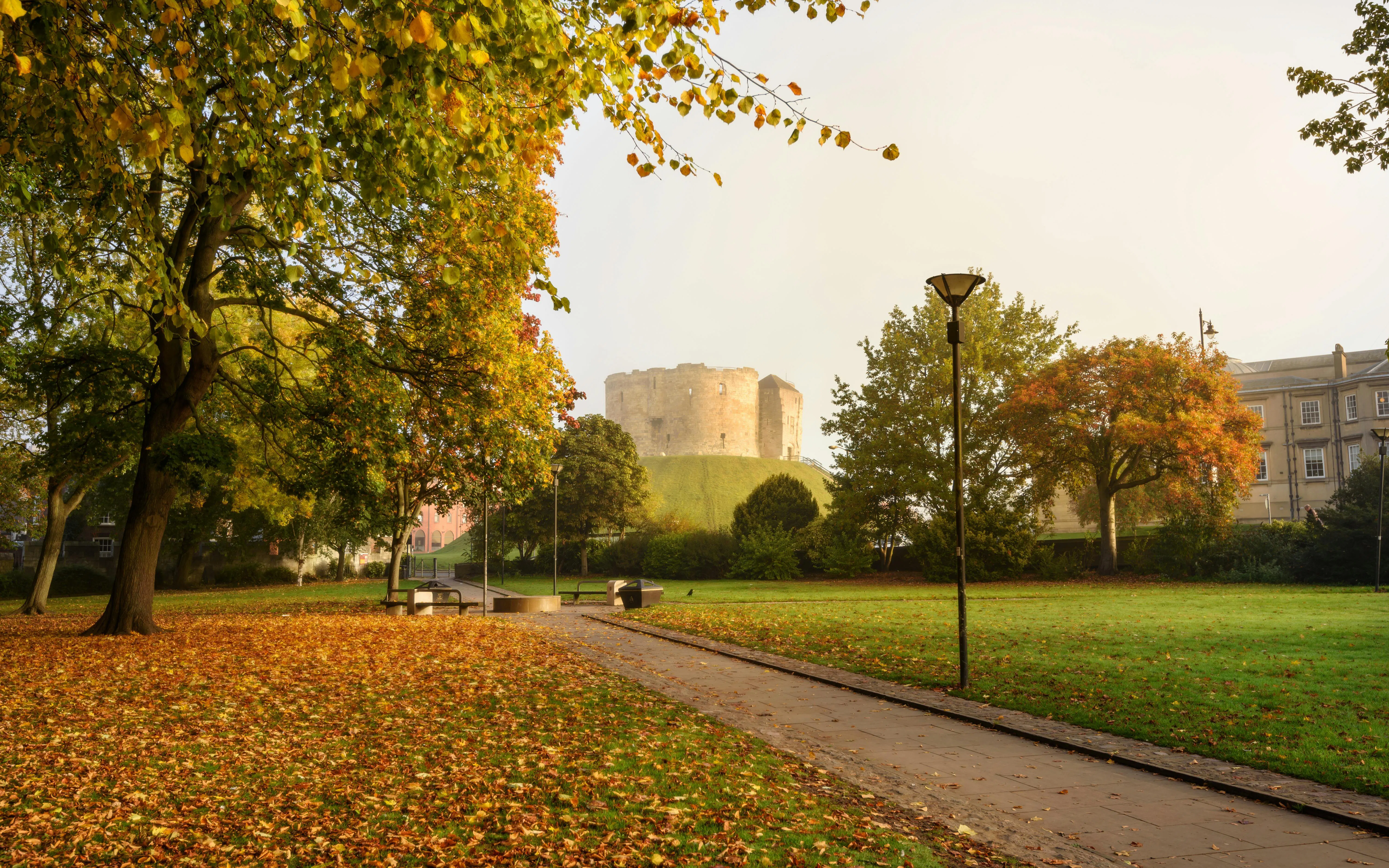 Clifford's Tower in York surrounded by autumn trees and a grassy park.