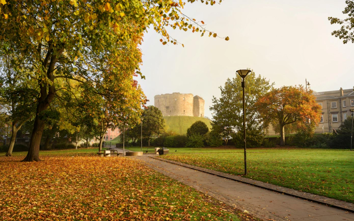 Clifford's Tower in York surrounded by autumn trees and a grassy park.