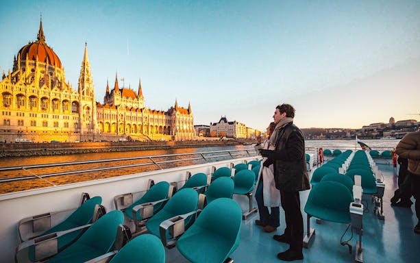 Guests enjoying Budapest Sunset Cruise with view of Hungarian Parliament Building.