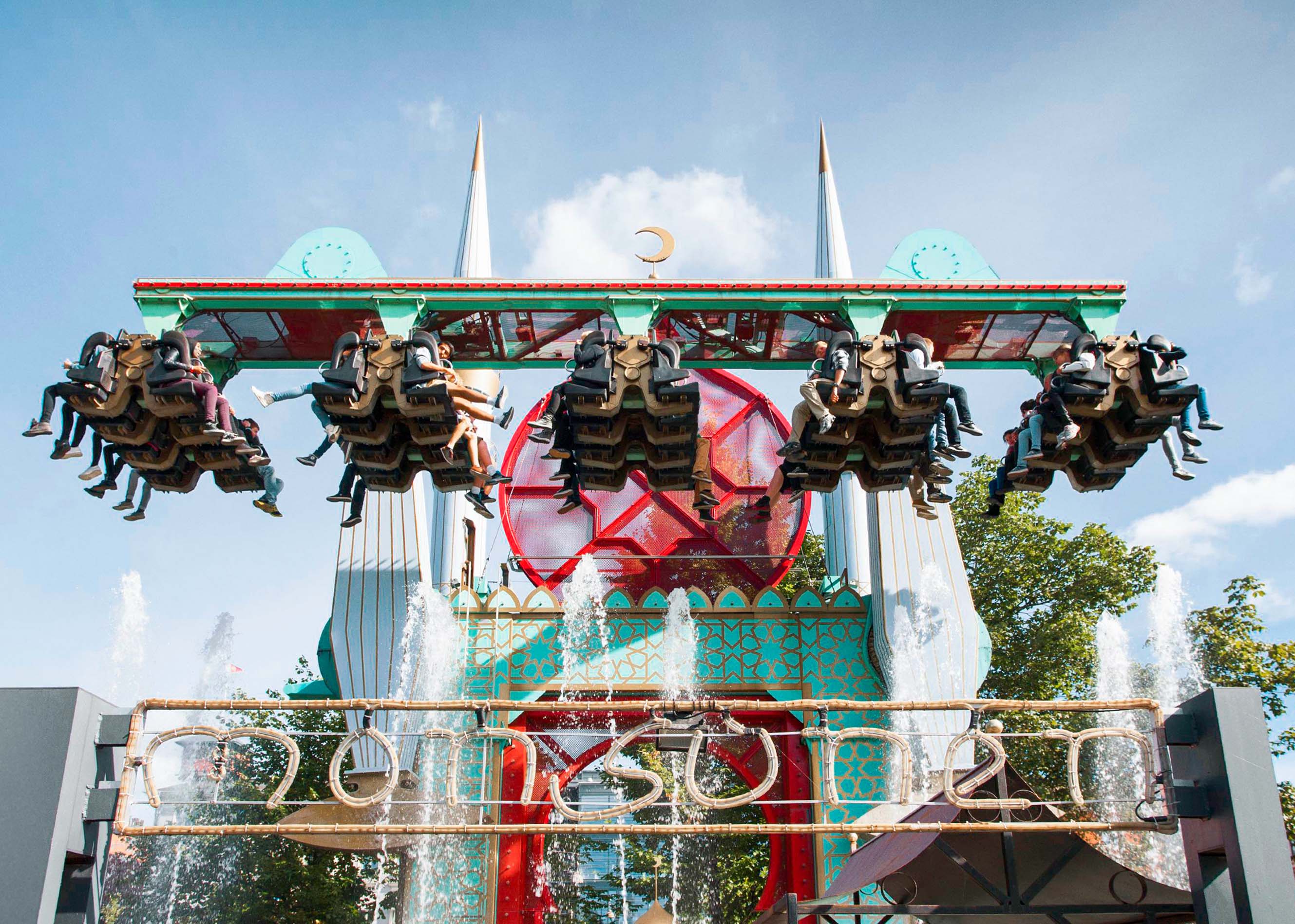 Visitors enjoying a vibrant evening at Tivoli Gardens, Copenhagen, with illuminated rides and lush greenery