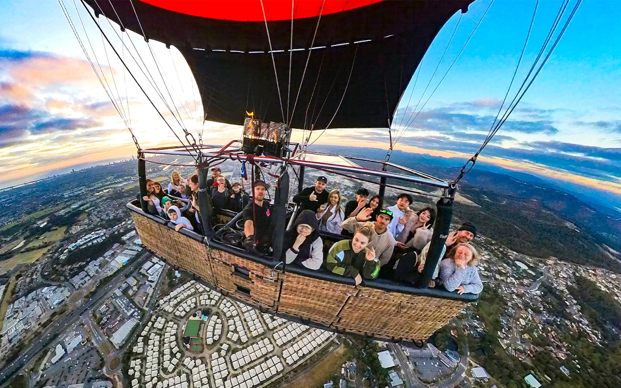 Group enjoying a hot air balloon flight over a cityscape at sunrise.