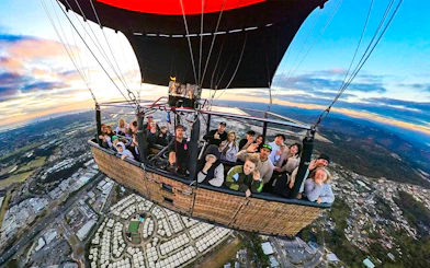 Group enjoying a hot air balloon flight over a cityscape at sunrise.
