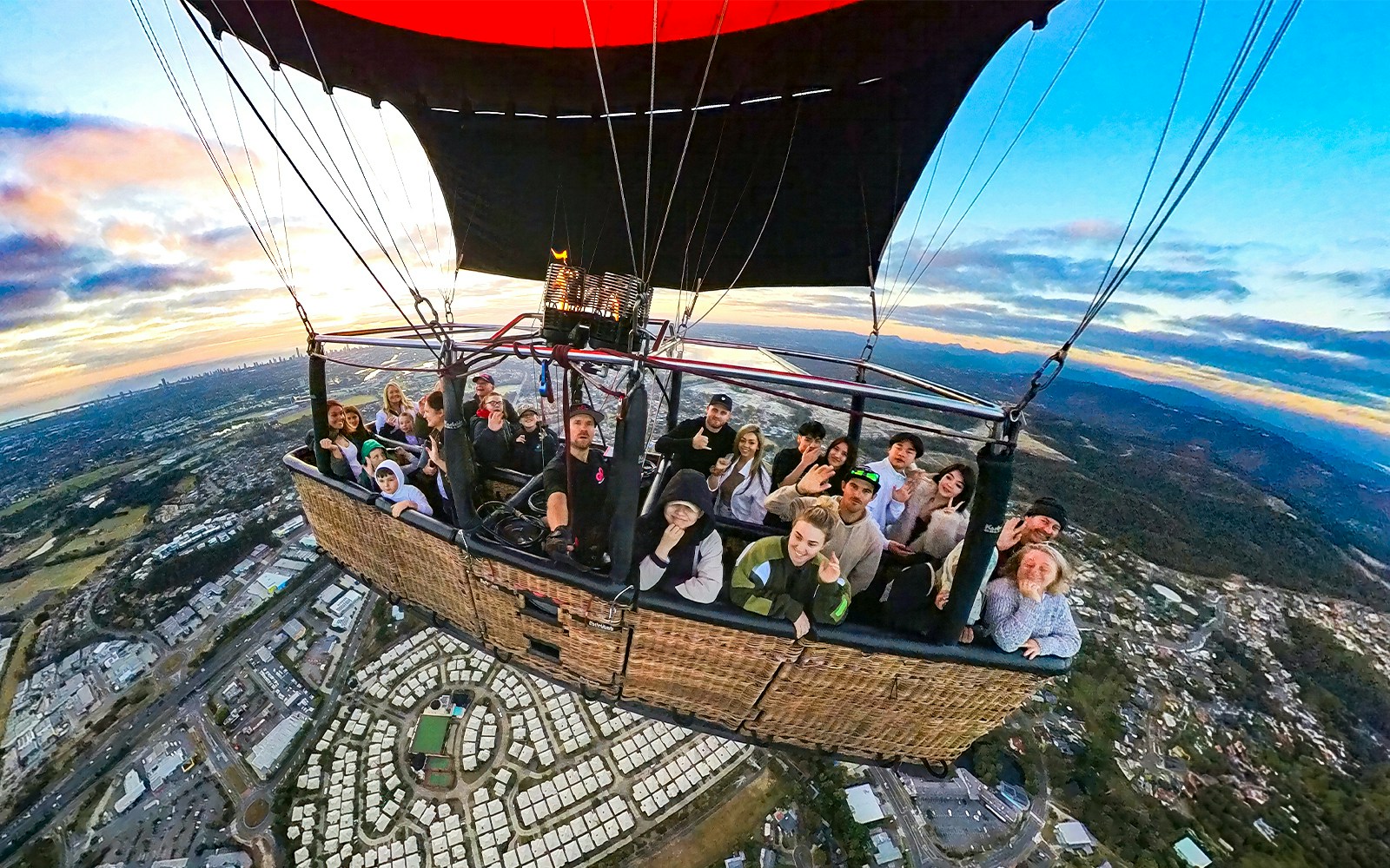 Group enjoying a hot air balloon flight over a cityscape at sunrise.