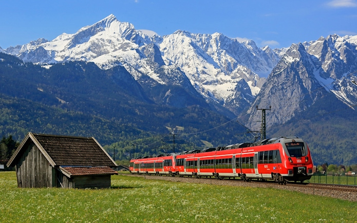 Local train traveling through scenic German landscape with snow-capped mountains.