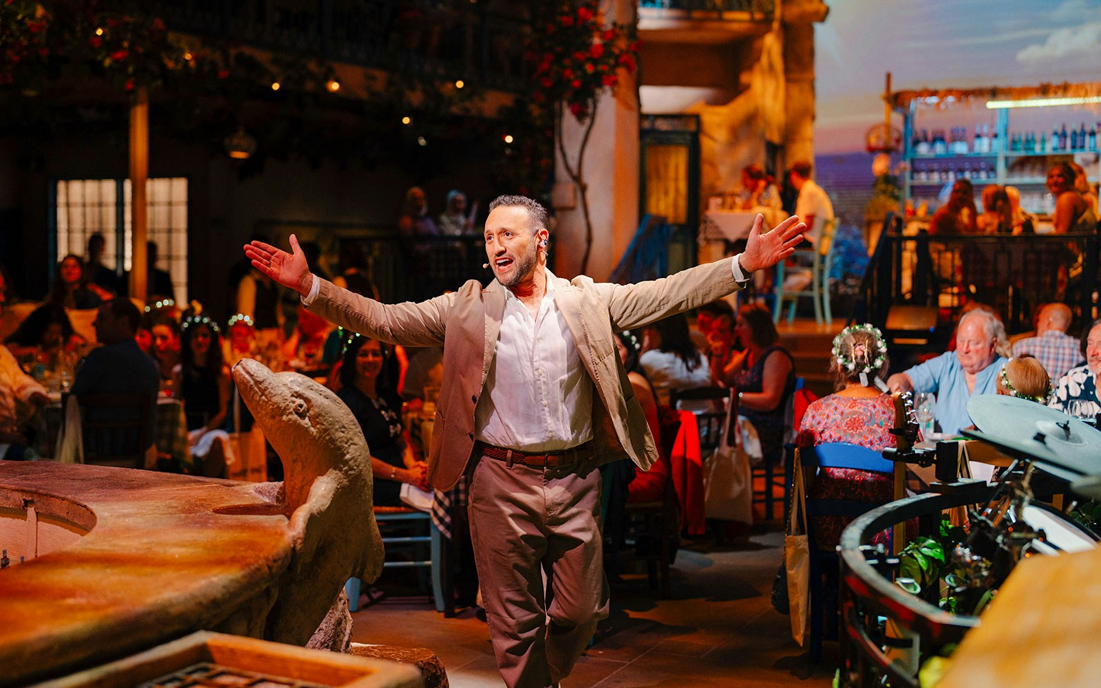 Performer engaging audience at Mamma Mia! The Party event with Mediterranean decor.