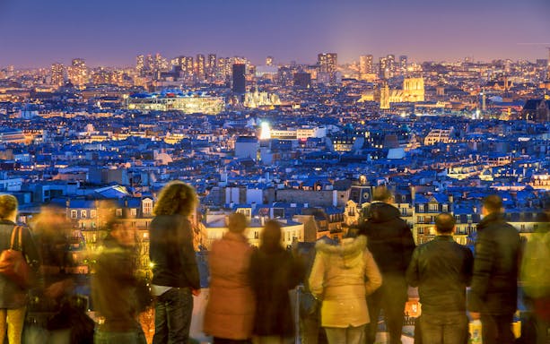 Montmartre view of Paris skyline at night with people on a walking tour.