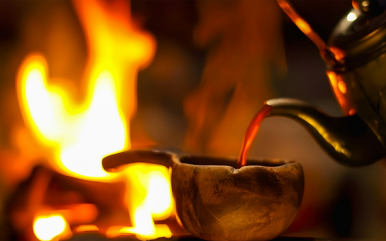Warm drink being poured into a wooden cup by a fire during Northern Lights tour.