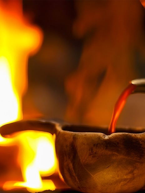 Warm drink being poured into a wooden cup by a fire during Northern Lights tour.