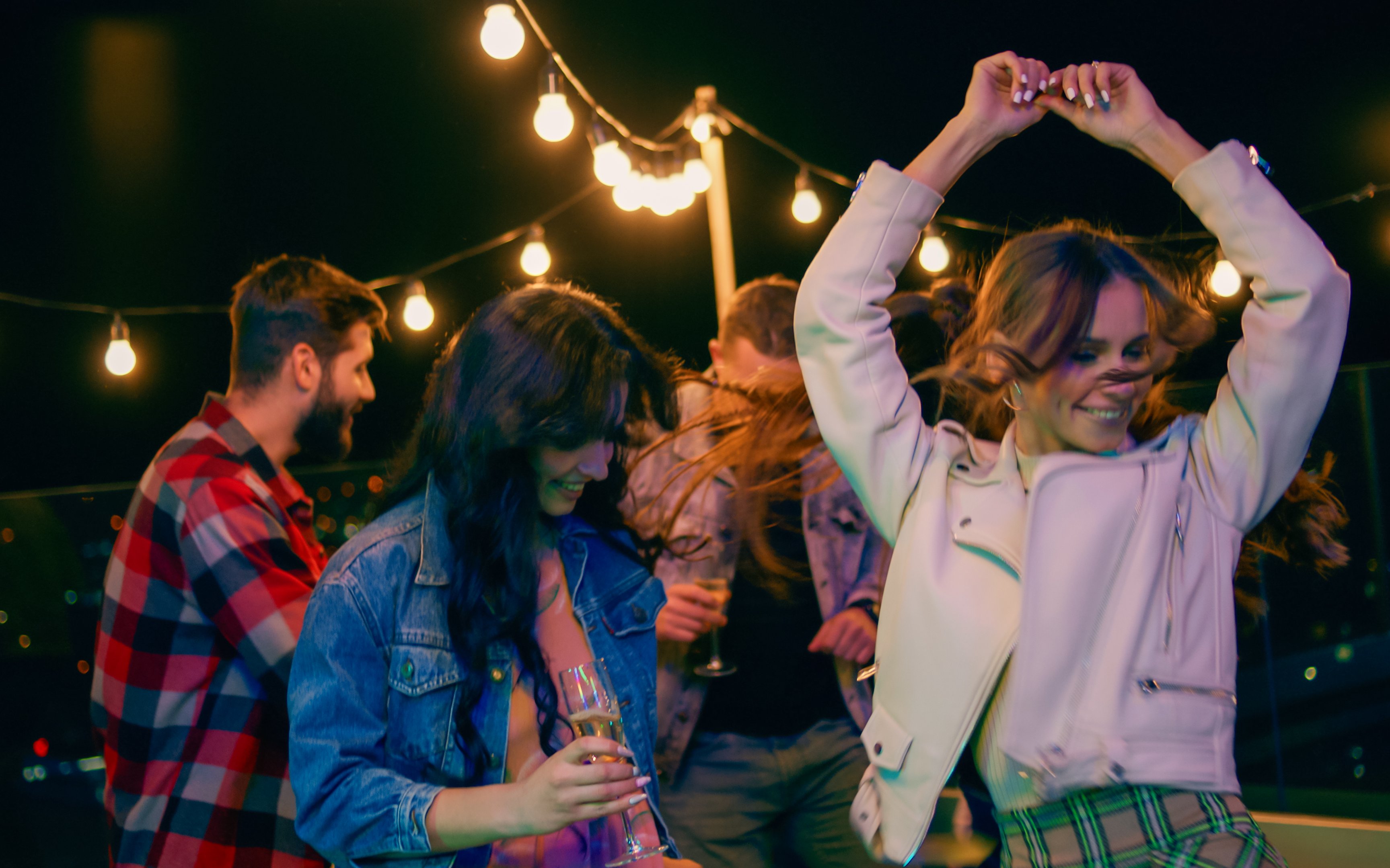 People dancing at a rooftop party under string lights at night.