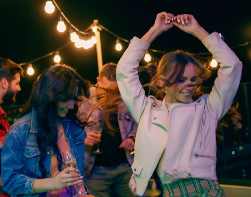 People dancing at a rooftop party under string lights at night.