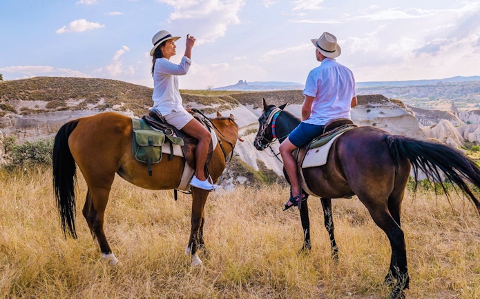 Guests horseback riding in Cappadocia with scenic rock formations in the background.