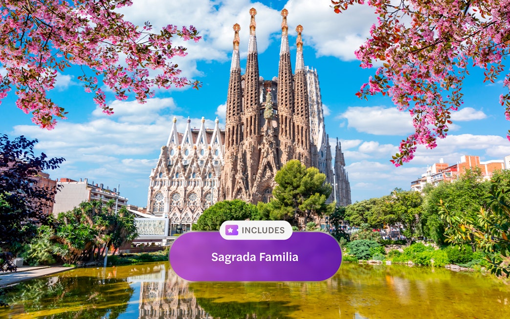 Sagrada Familia in Barcelona with blooming trees and reflection in pond.