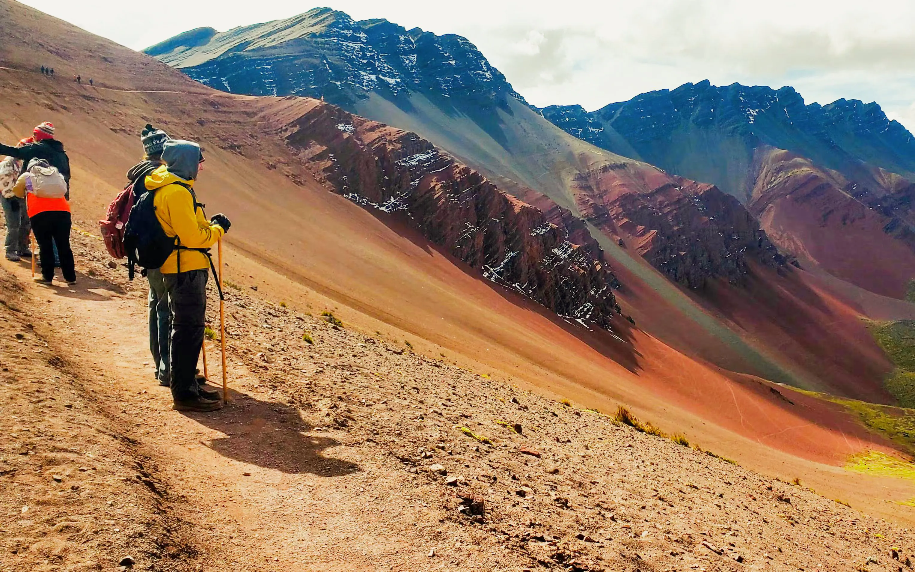 Hikers on a trail with Rainbow Mountain and Red Valley in the background, Peru.