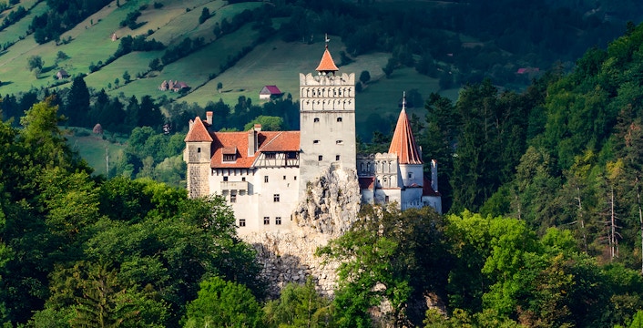 Bran Castle in Romania surrounded by lush greenery and distant hills.