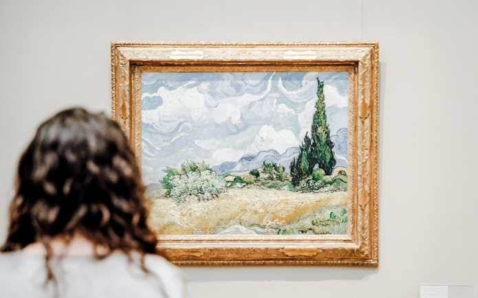 Viewer admiring Vincent van Gogh's "Wheat Field with Cypresses" painting.