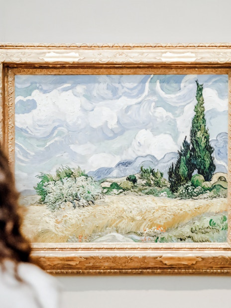 Viewer admiring Vincent van Gogh's "Wheat Field with Cypresses" painting.