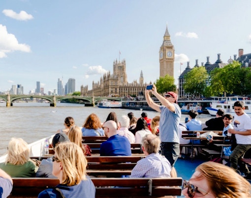 Tourists on a cruise near the Thames River photographing Big Ben and the Houses of Parliament.