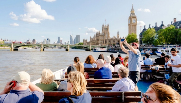 Tourists on a cruise near the Thames River photographing Big Ben and the Houses of Parliament.