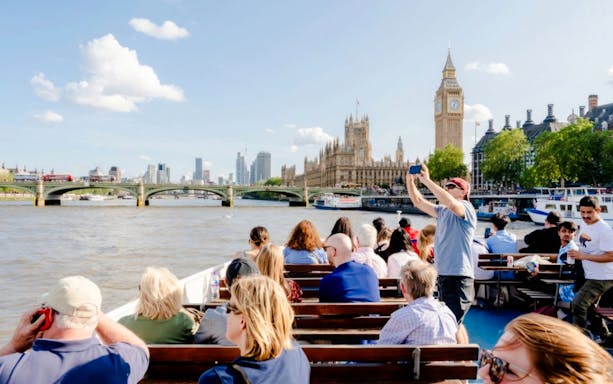 Tourists on a cruise near the Thames River photographing Big Ben and the Houses of Parliament.