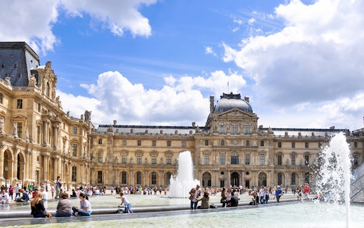 Louvre Museum courtyard with fountains and visitors in Paris.