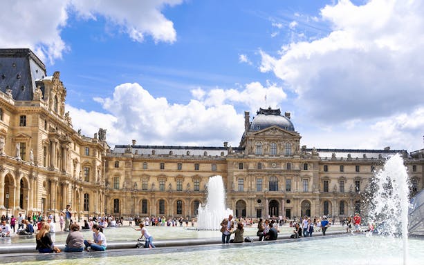 Louvre Museum courtyard with fountains and visitors in Paris.