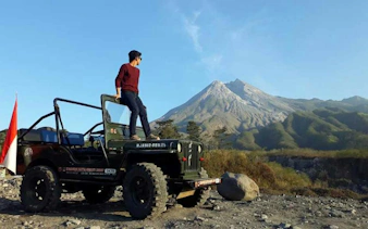 Jeep tour at sunrise near Mount Merapi, Indonesia, with a person standing on the vehicle.