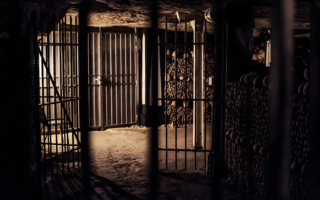 Dimly lit catacombs corridor with gated entrance and stacked bones, Paris tour.