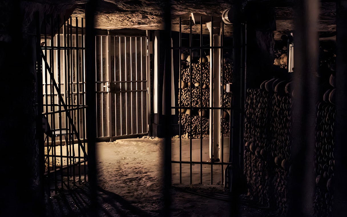 Dimly lit catacombs corridor with gated entrance and stacked bones, Paris tour.