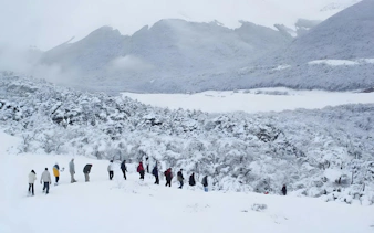 Group hiking through snowy landscape in Ushuaia with mountains in the background.